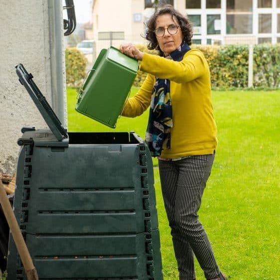 women putting things to compost into a compost bin with a thought full look