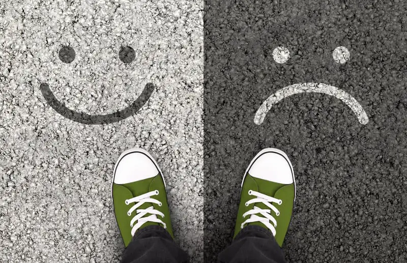 someone looking down on a pavement with a drawing of one happy face and one unhappy face