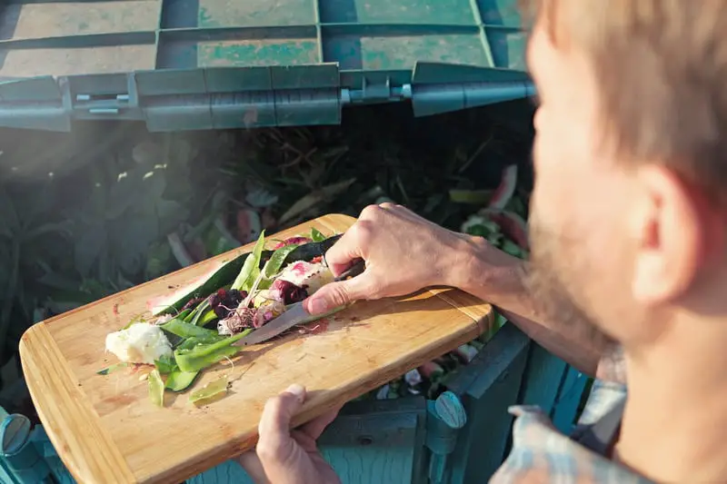 man scraping scraps on a chopping board into a compost bin