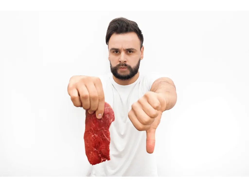 man holding meat in one hand and thumbs down with other hand in a white tee shirt and white background