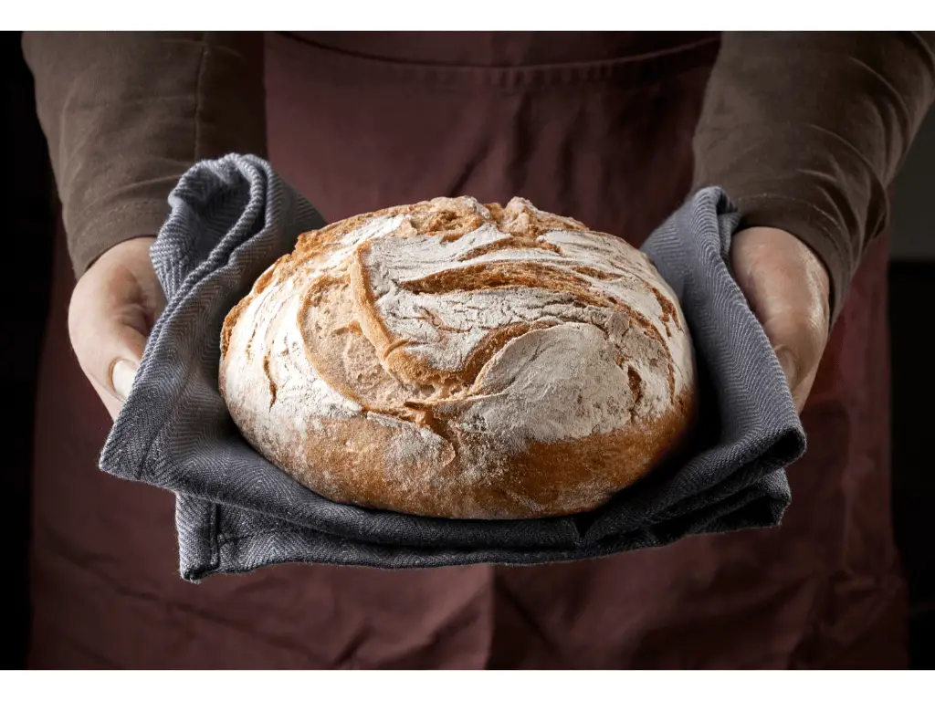 person holding freshly baked bread with a kitchen towel 