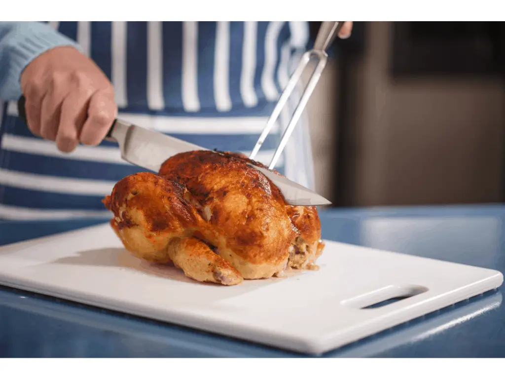 person cutting into a cooked chicken with a chefs knife