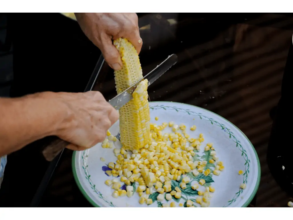 person slicing into a corn cob with a knife