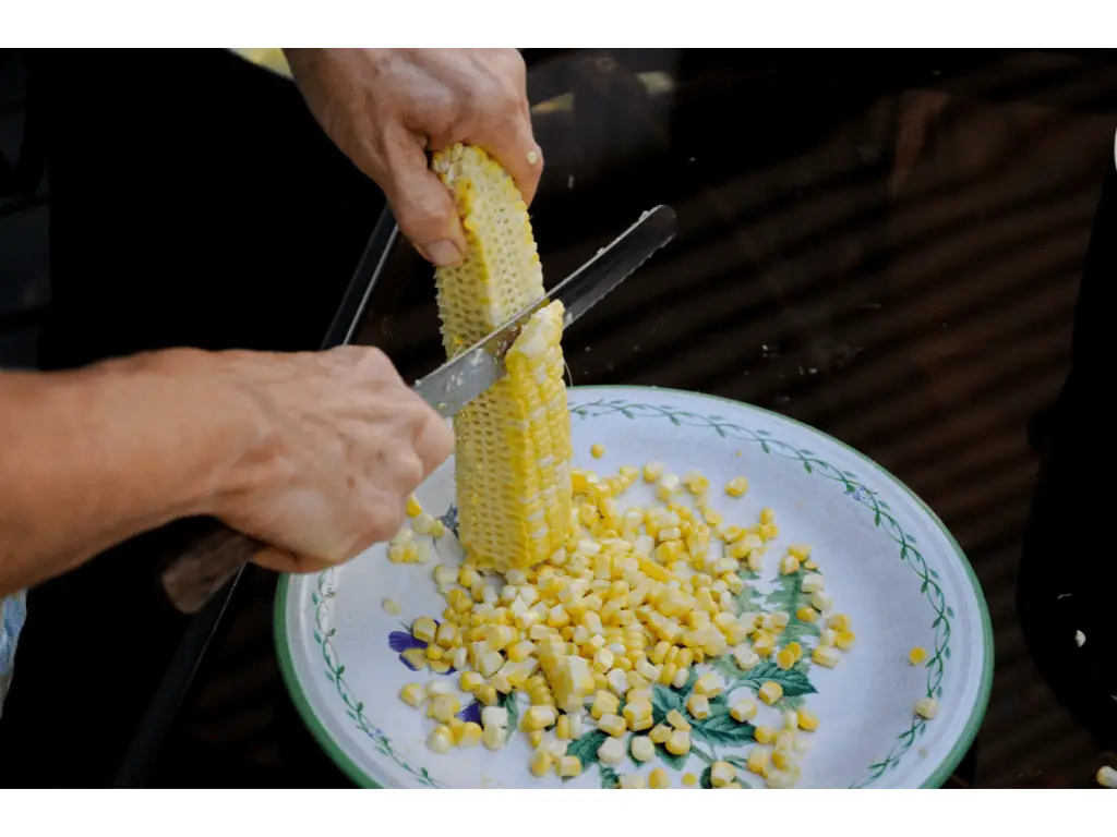 person slicing into a corn cob with a knife