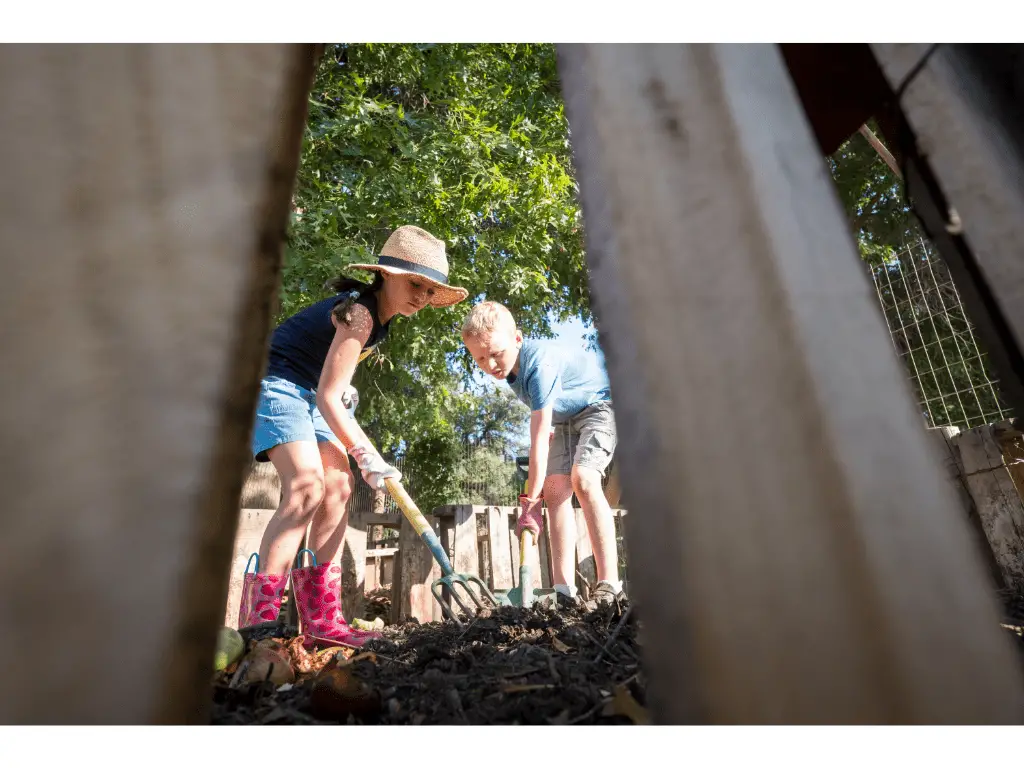 children turning compost with a garden folk in a garden