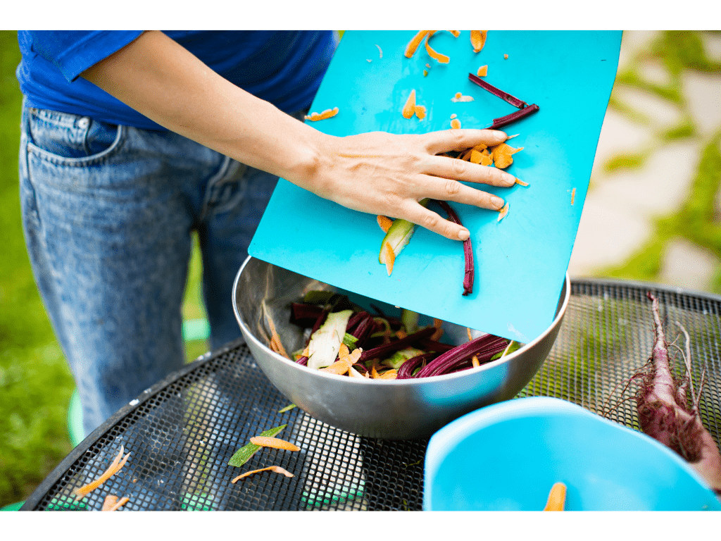 person putting vegetable scraps the a compost bin